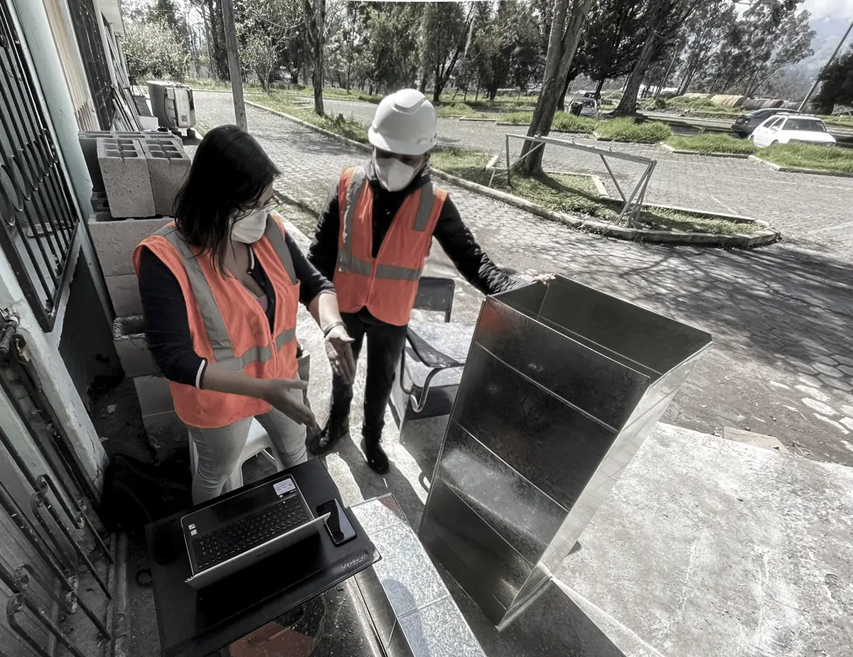 Dos personas con chaleco de seguridad revisan una pieza de ducto en una obra